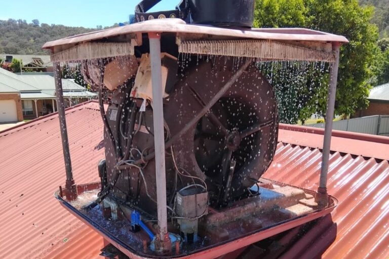 Evaporative air conditioner on a red metal roof in Albury Wodonga being serviced, showing internal fan, water flow, and cooling pads in operation.