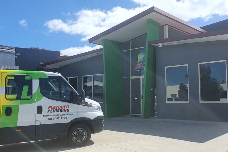 Fletcher Plumbing van parked outside the Fletcher Plumbing and Co building in Albury, showing the company signage, green exterior pillars and clear blue sky.
